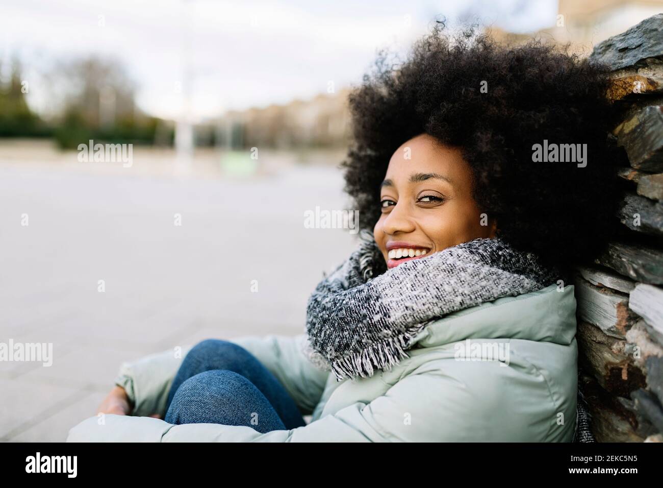 Sorridente giovane donna in abiti caldi mentre si siede all'aperto Foto Stock