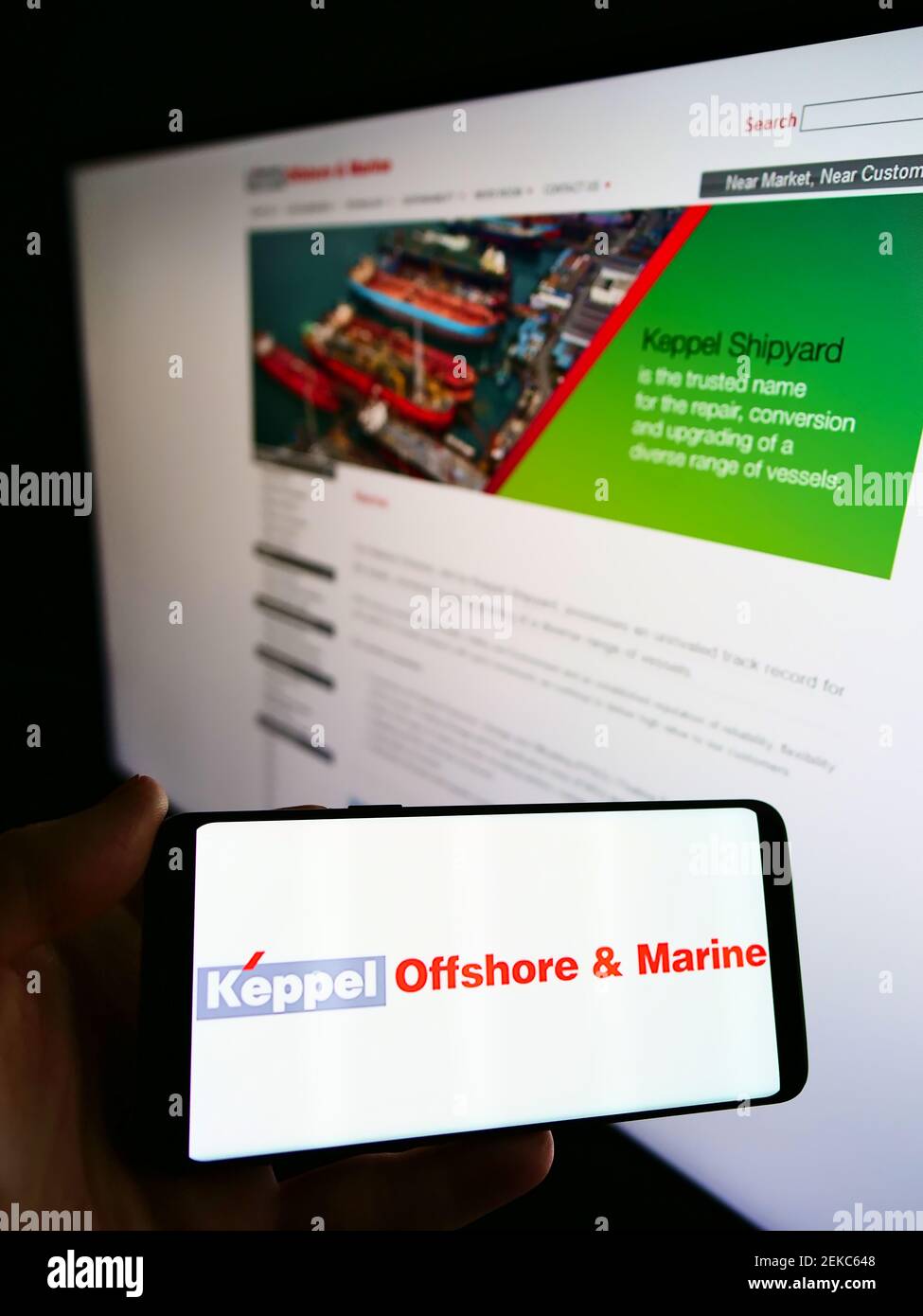 Persona che detiene il telefono cellulare con il logo della società singaporiana Keppel Offshore e Marine sullo schermo di fronte alla pagina web. Focus sul display del cellulare. Foto Stock