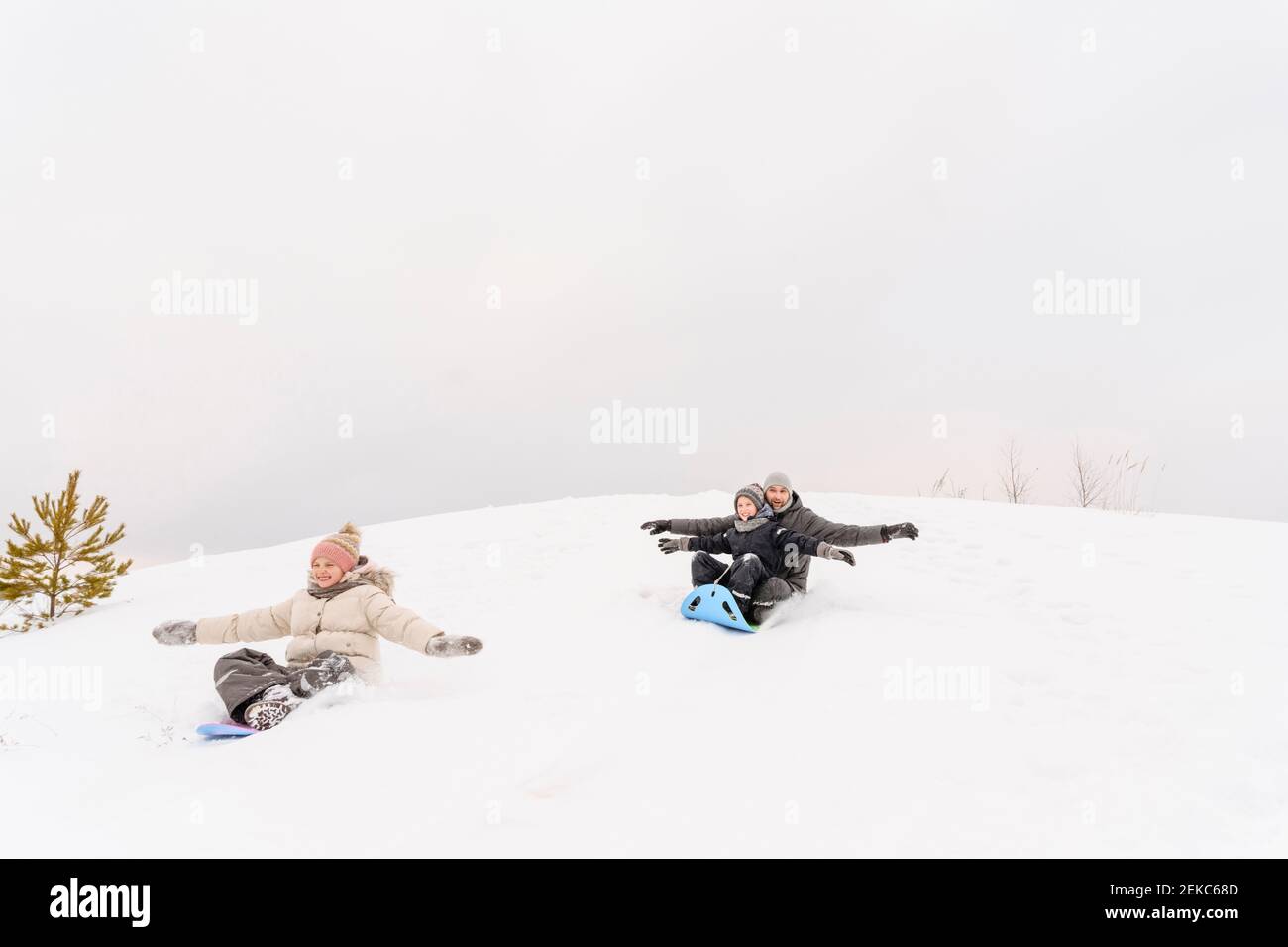 Il padre giocoso con i bambini che dormono sulla collina nevosa contro il cielo durante le vacanze Foto Stock