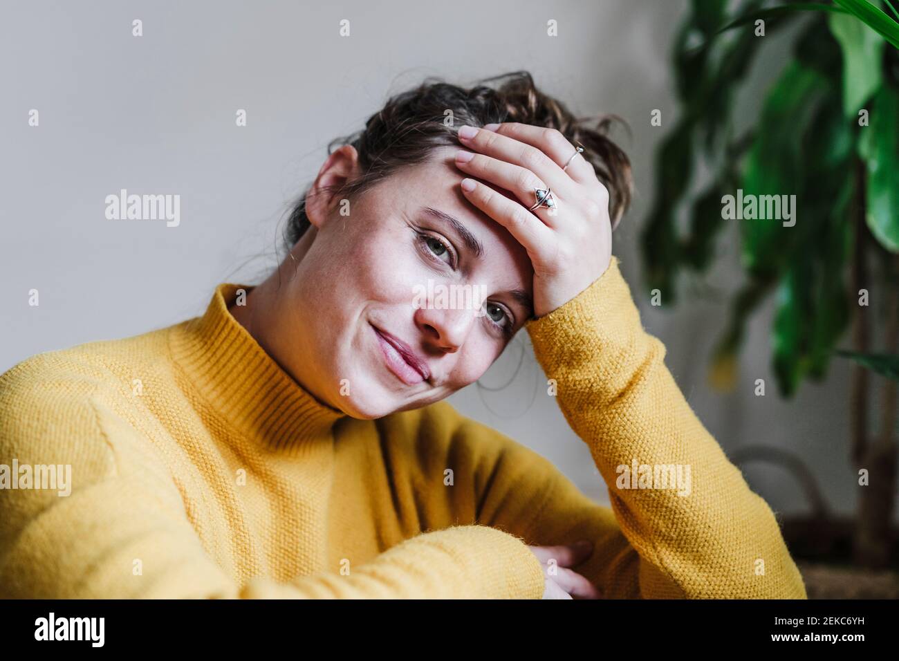 Donna sorridente con testa in mani che fissano mentre si siede a. casa Foto Stock
