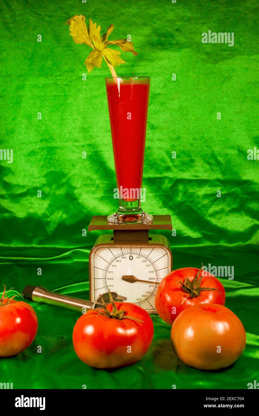 Bicchiere di succo su scala di peso da pomodori freschi contro tessuto verde Foto Stock