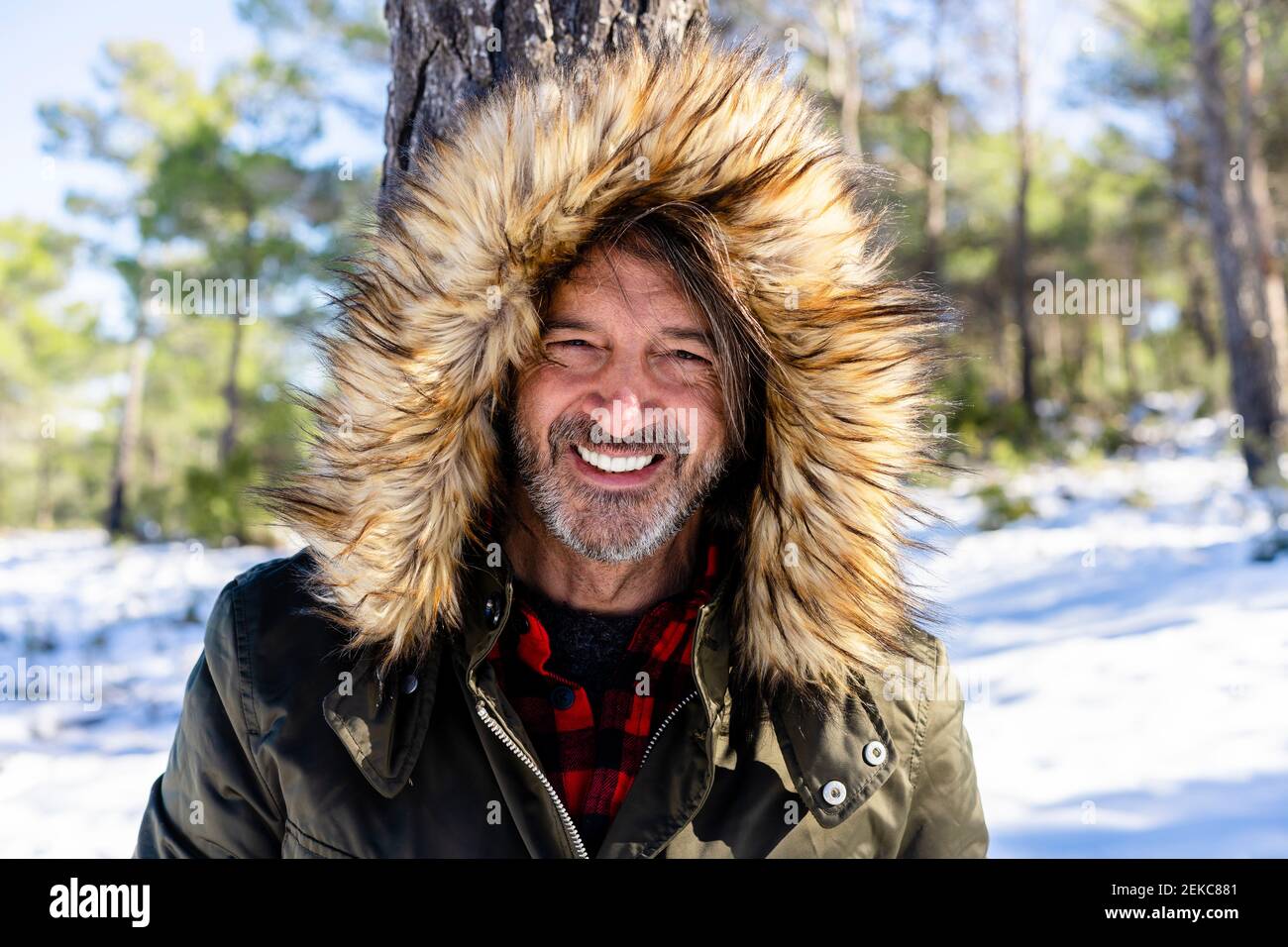 Uomo maturo con cappuccio in pelliccia sorridente mentre si trova in piedi nella foresta Foto Stock