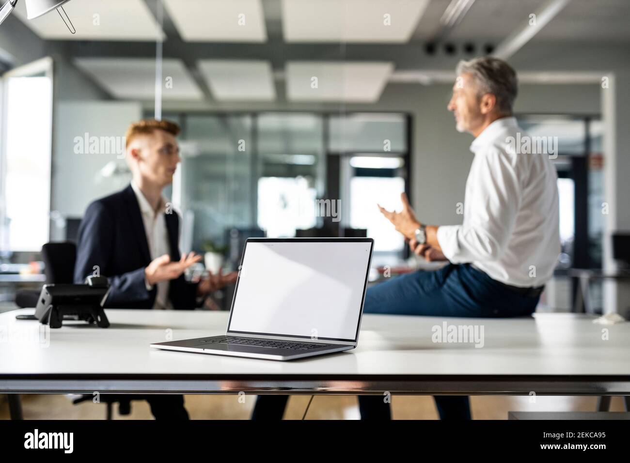 Laptop sul tavolo con persone aziendali che hanno discussioni in background presso un ufficio open plan Foto Stock