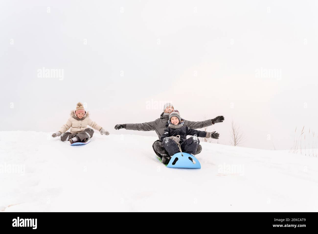 Il padre giocoso con i bambini che dormono sulla collina nevosa contro il cielo Foto Stock