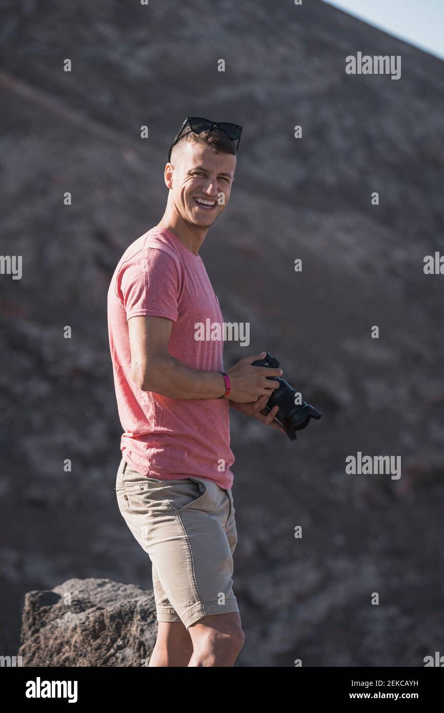 Felice turista maschio tenendo macchina fotografica a Femes Viewpoint in giornata di sole, Lanzarote, Spagna Foto Stock