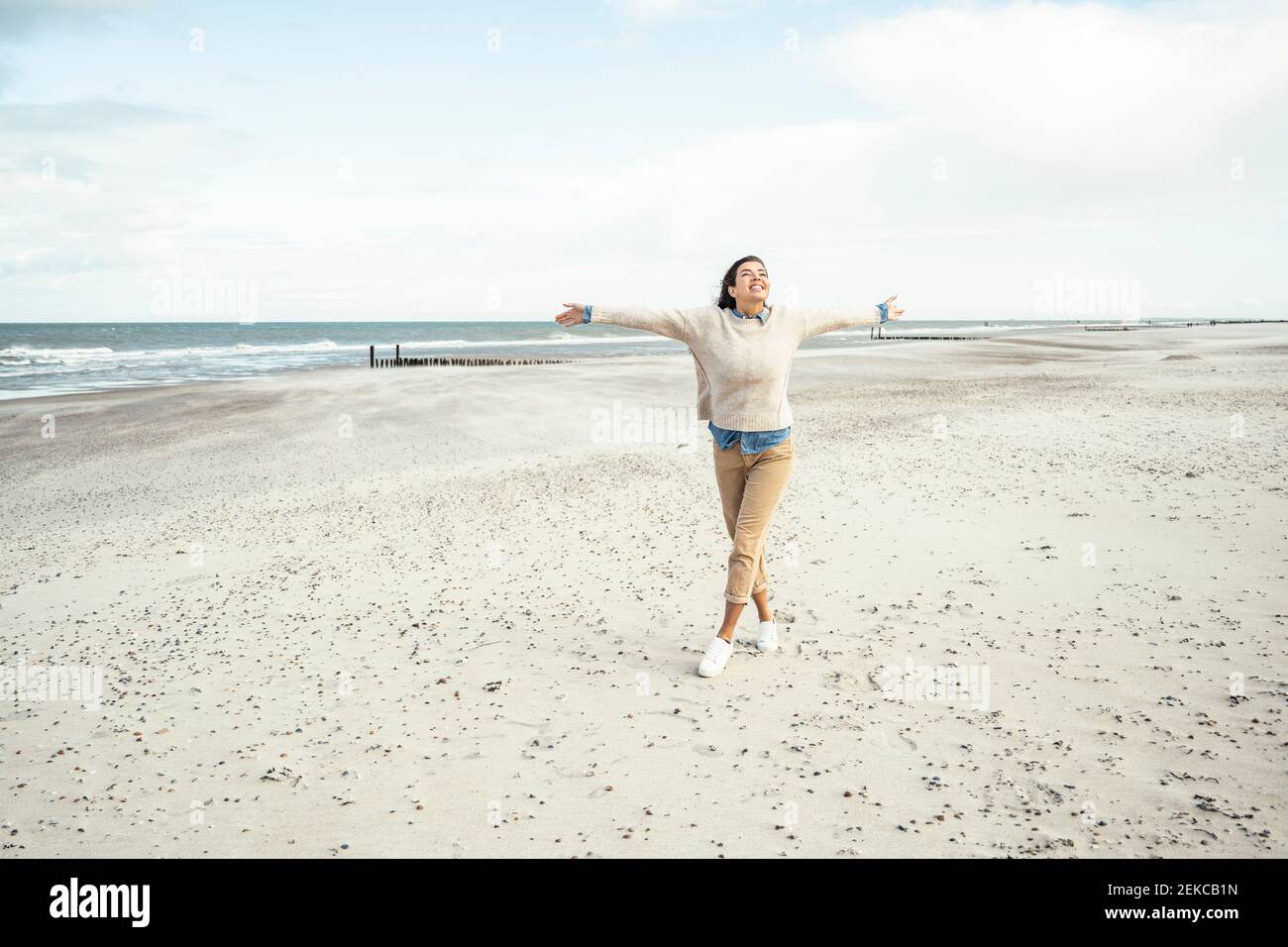 Ritratto di giovane donna che cammina sulla spiaggia di sabbia con rialzato braccia Foto Stock