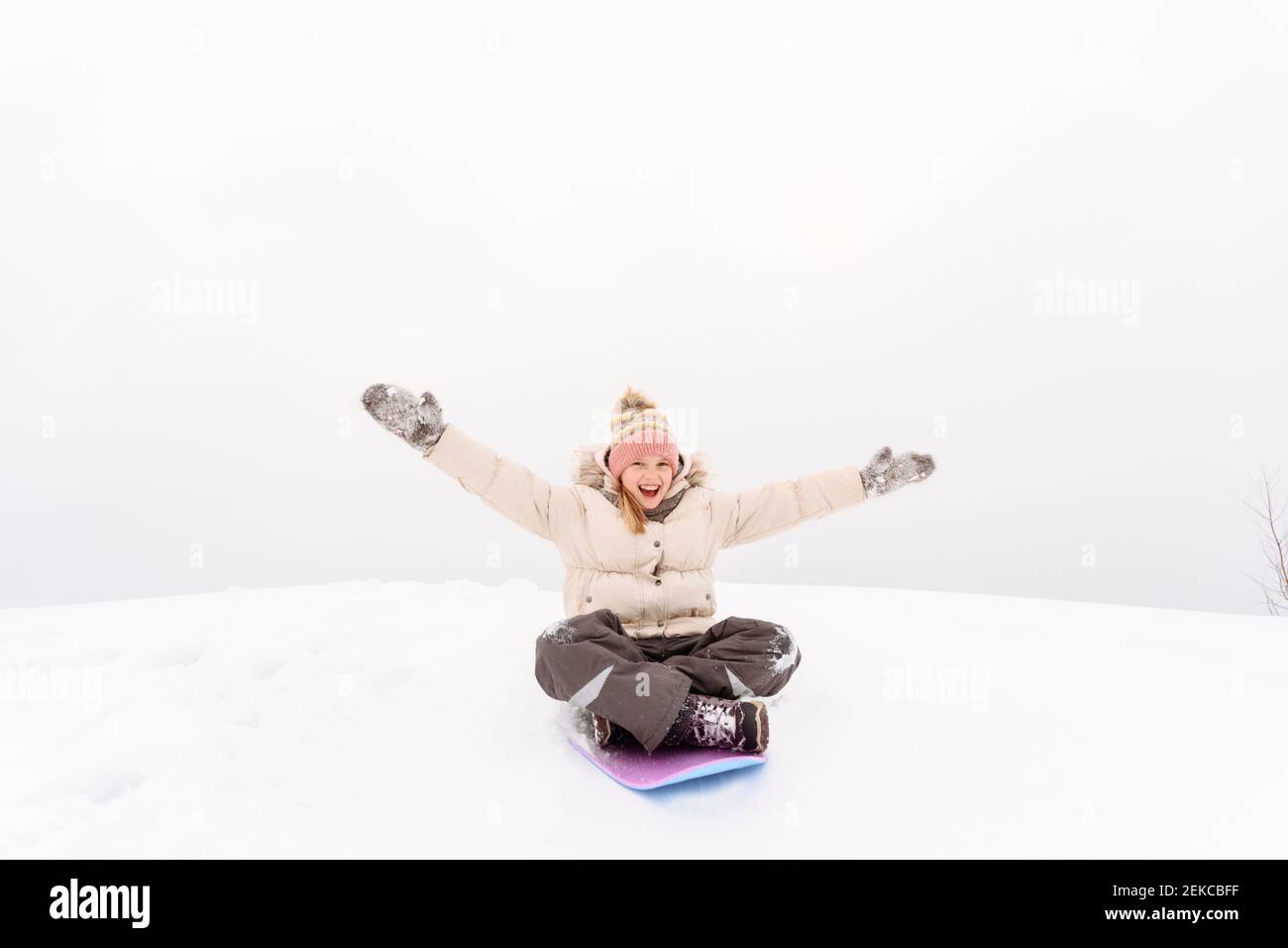 Ragazza spensierata con le braccia allungate sledding su collina nevosa contro cielo Foto Stock