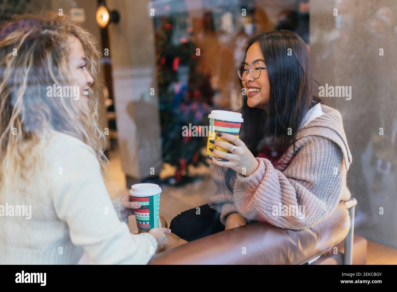 Giovani amici donne che hanno caffè mentre si siede in un bar visto attraverso il vetro del finestrino Foto Stock