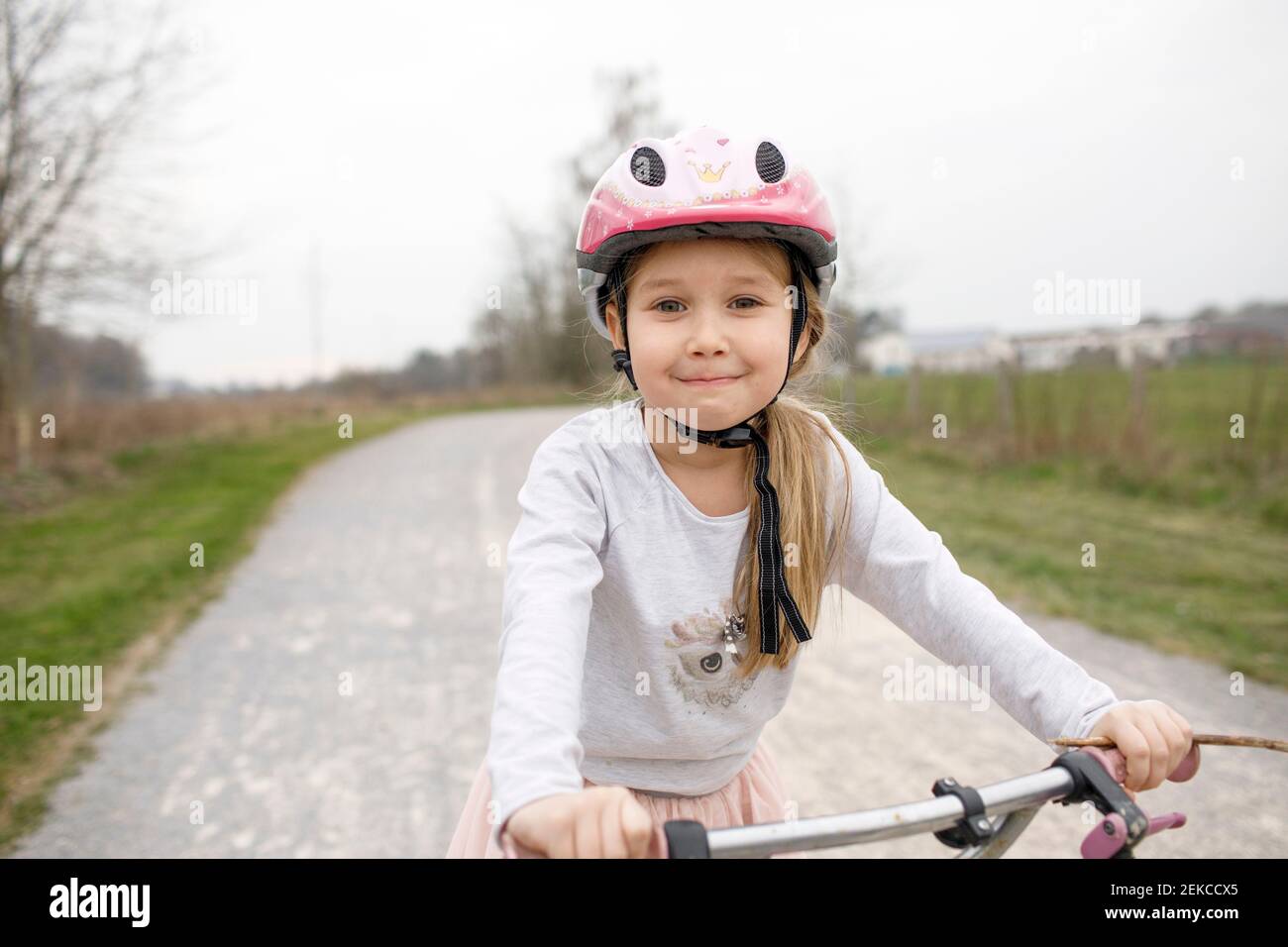 Ragazza sorridente in bicicletta che indossa il casco da ciclismo Foto Stock