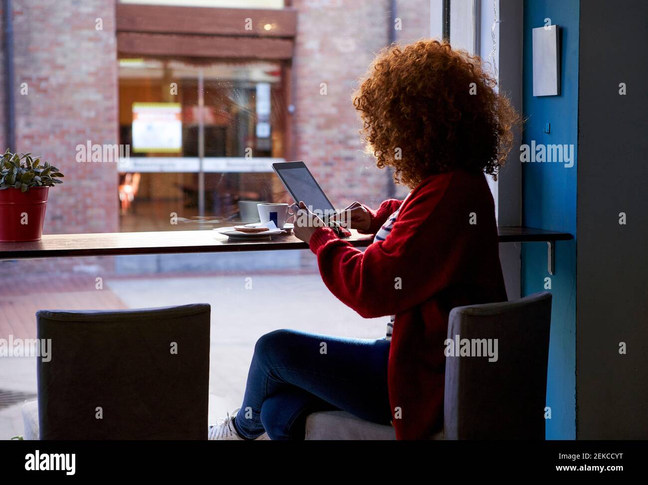 Giovane donna che usa un tablet digitale mentre si siede al bar Foto Stock