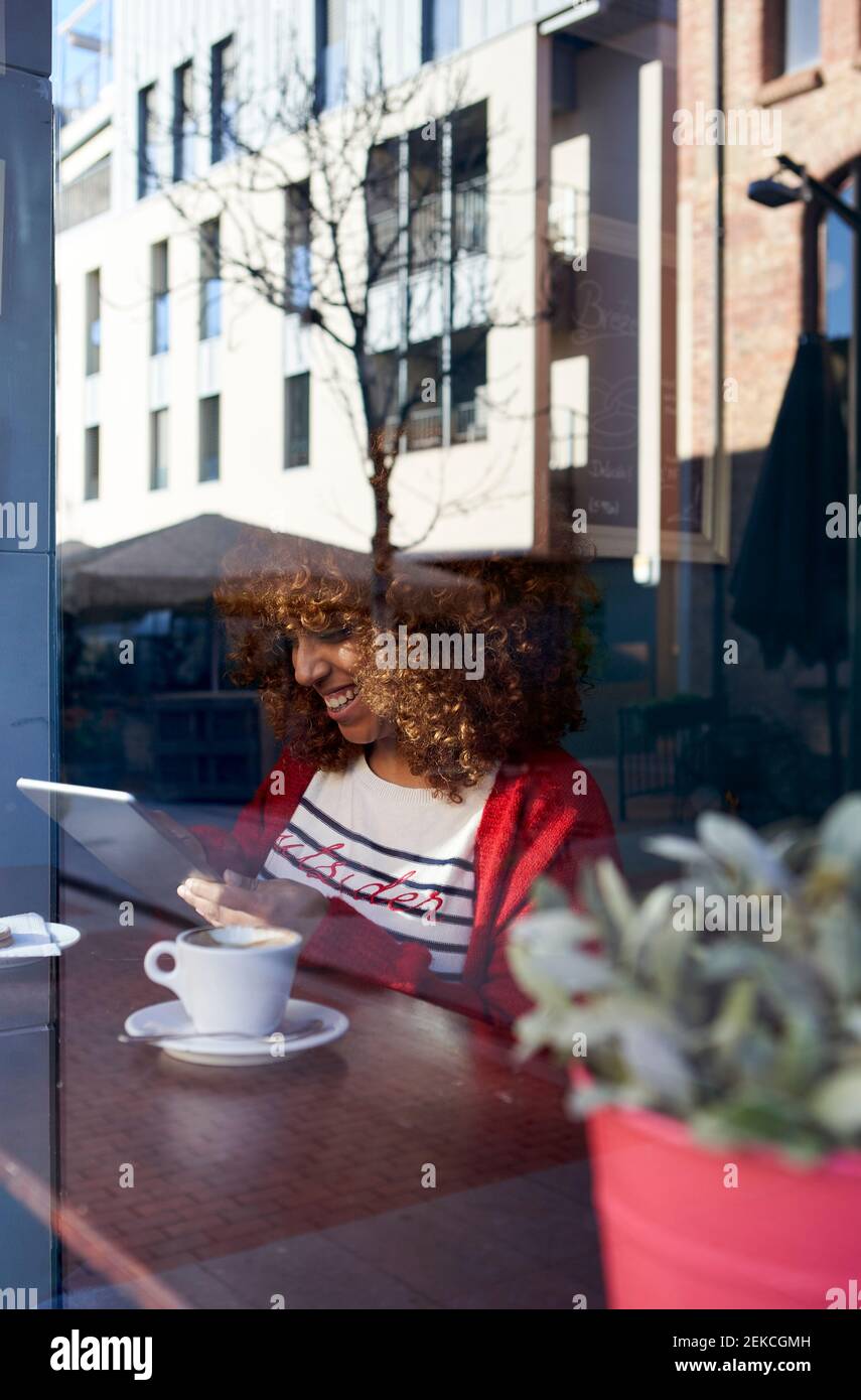 Giovane donna che usa il tablet digitale mentre si siede vicino alla finestra a. caffè Foto Stock