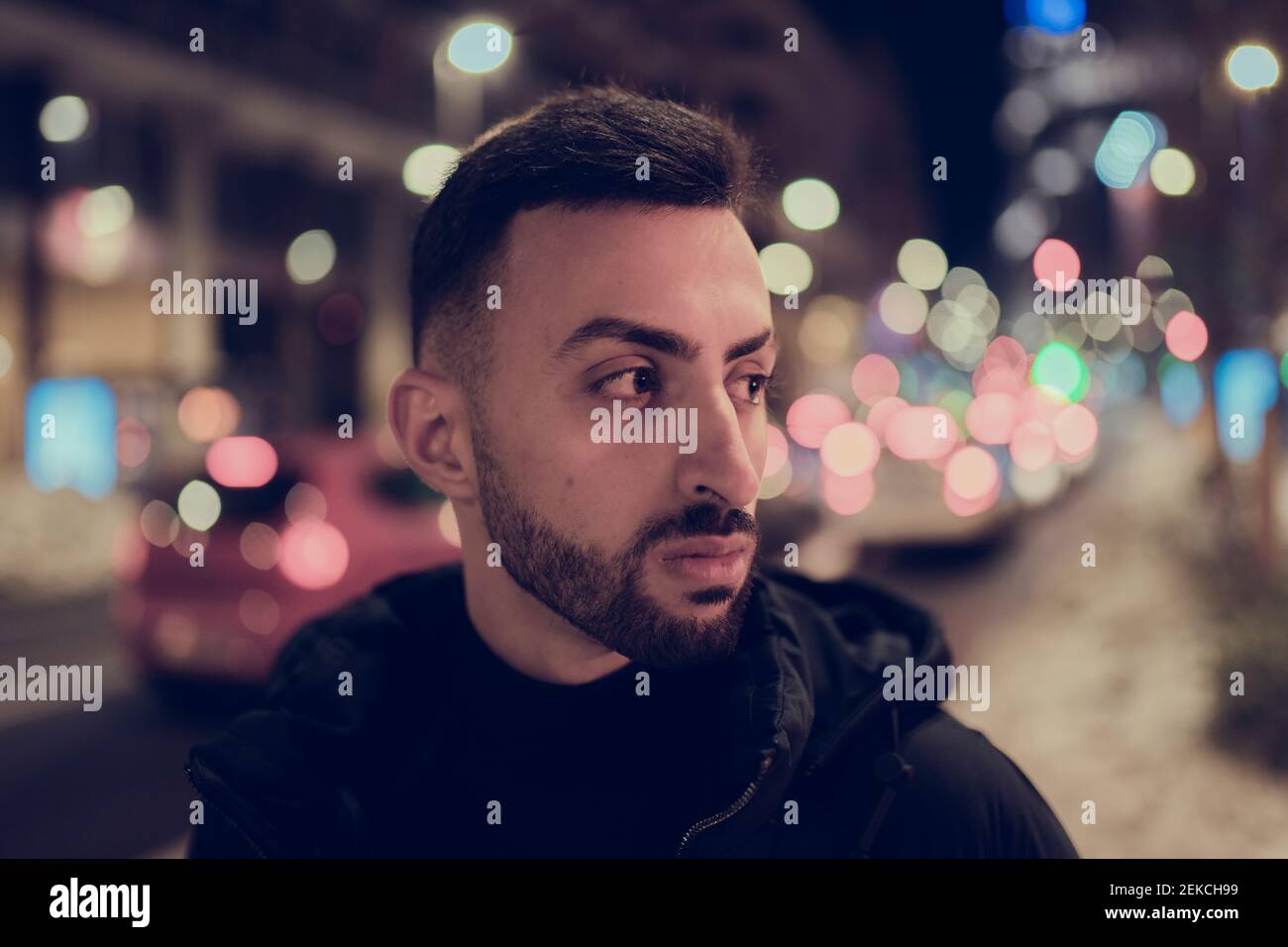 Contemplare il giovane uomo da una città illuminata mentre si guarda via notte Foto Stock