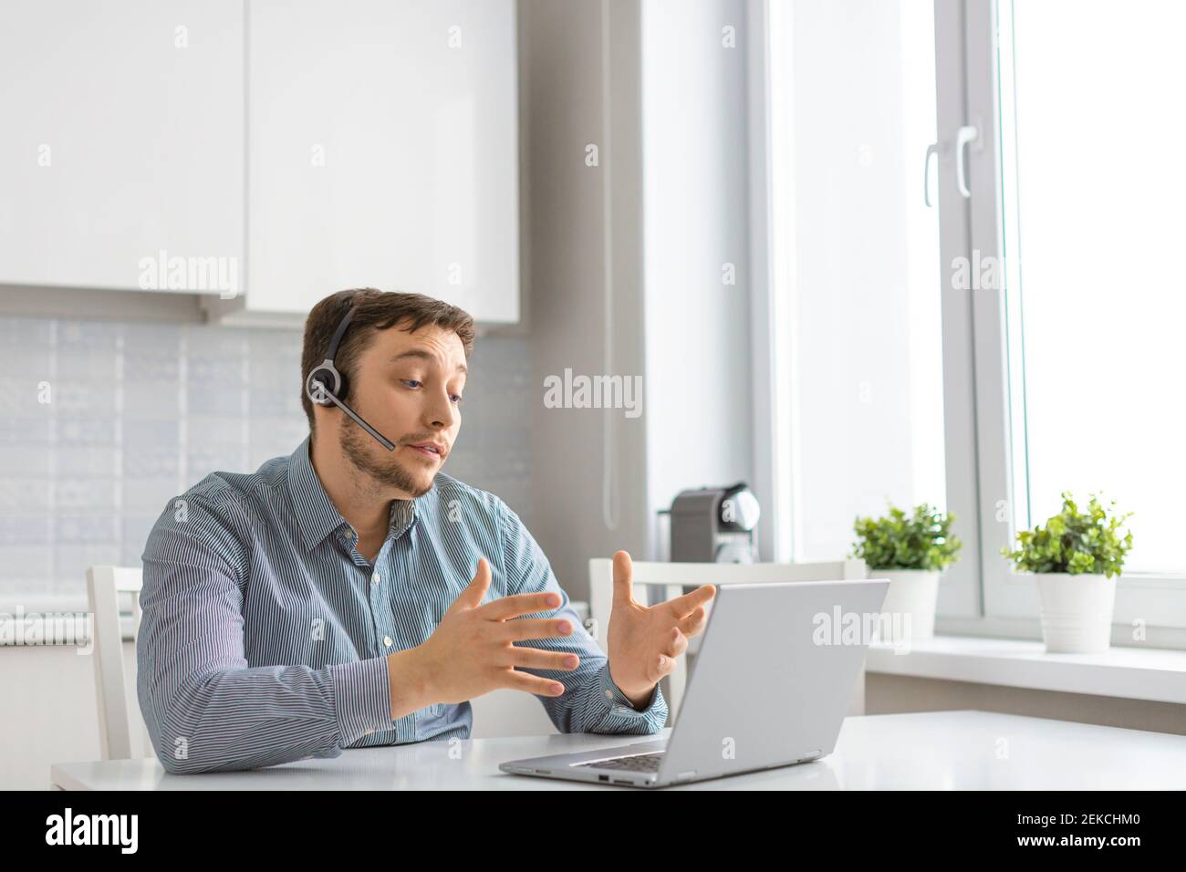 Un uomo durante una videochiamata online. Si siede a casa davanti al monitor di un computer portatile e parla utilizzando una cuffia. Concetto di tecnologie moderne per la comunità Foto Stock
