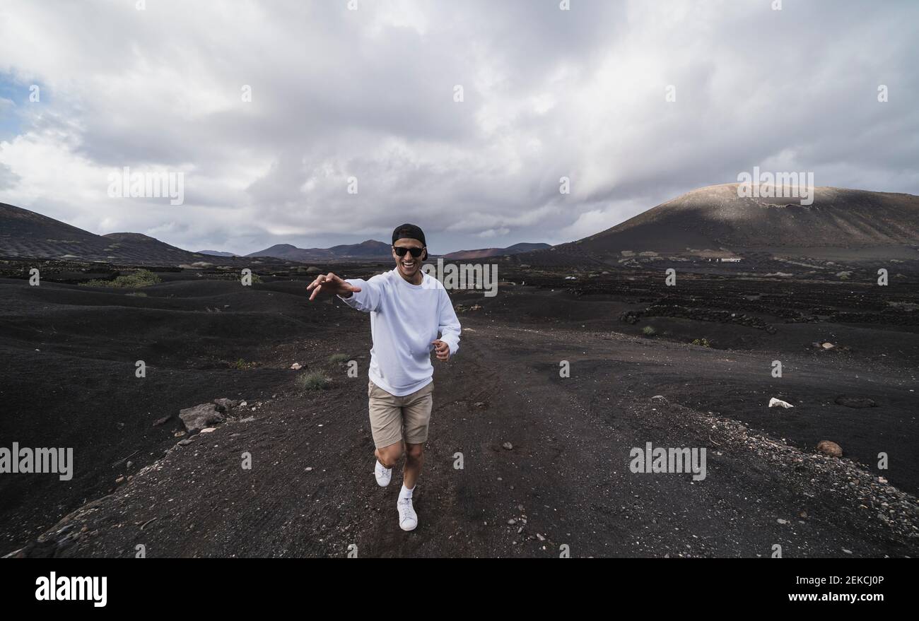 Sorridente turista maschile che corre mentre gesturando sul suolo nero al vulcano El Cuervo, Lanzarote, Spagna Foto Stock