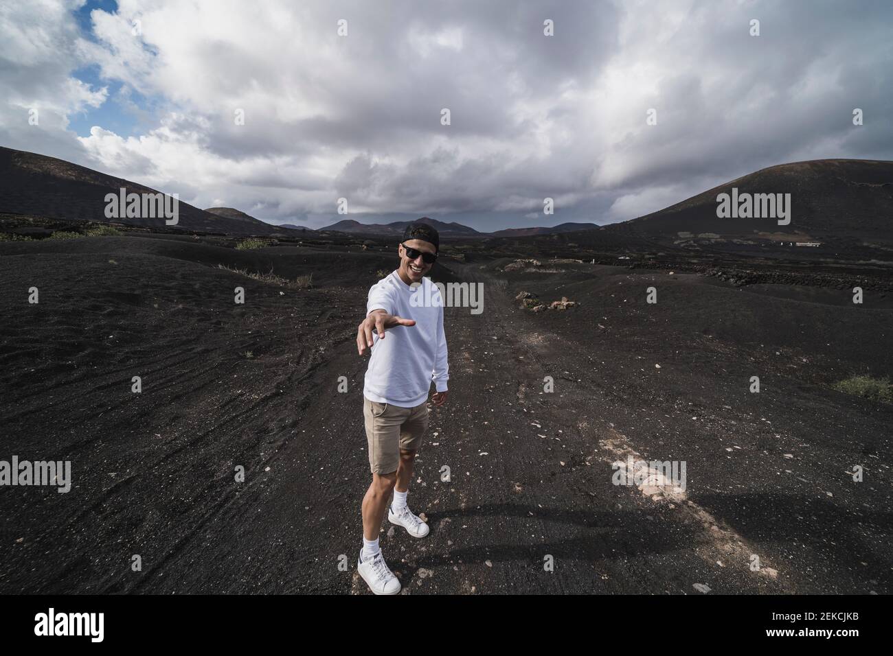 Sorridendo uomo turista gesturing mentre in piedi sul suolo nero al vulcano El Cuervo, Lanzarote, Spagna Foto Stock