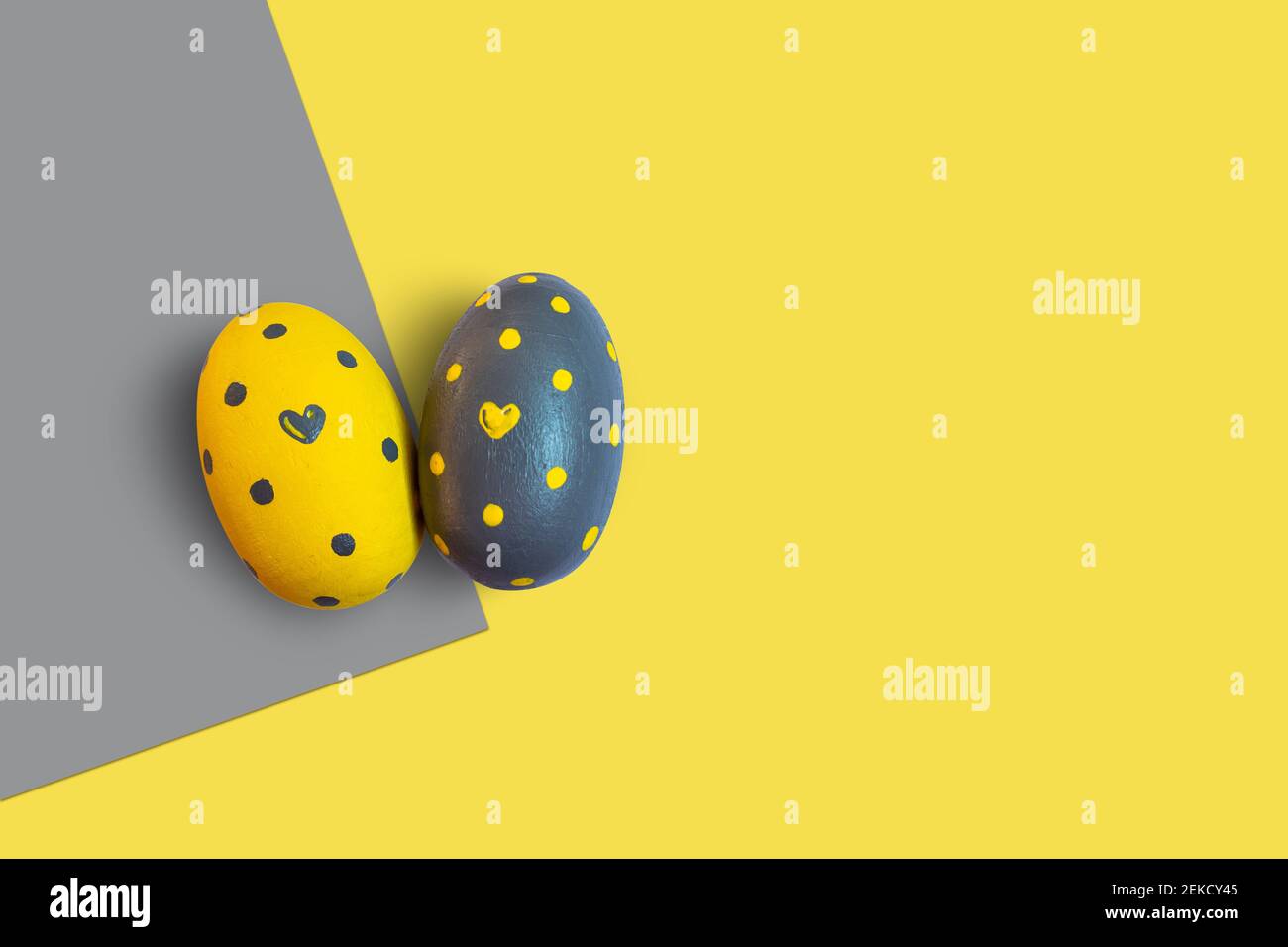 Pasqua in giallo illuminato e grigio estremo. Due uova decorate con cuori e puntini su uno sfondo bicolore. Foto Stock