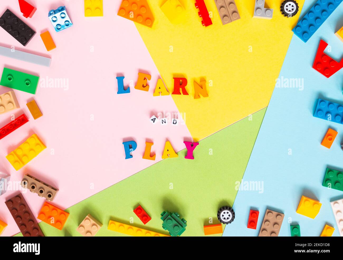 Parole fatte di lettere di legno multicolore 'imparare e giocare' su uno sfondo multicolore, kit di costruzione per bambini intorno. Vista dall'alto, spazio libero per Foto Stock