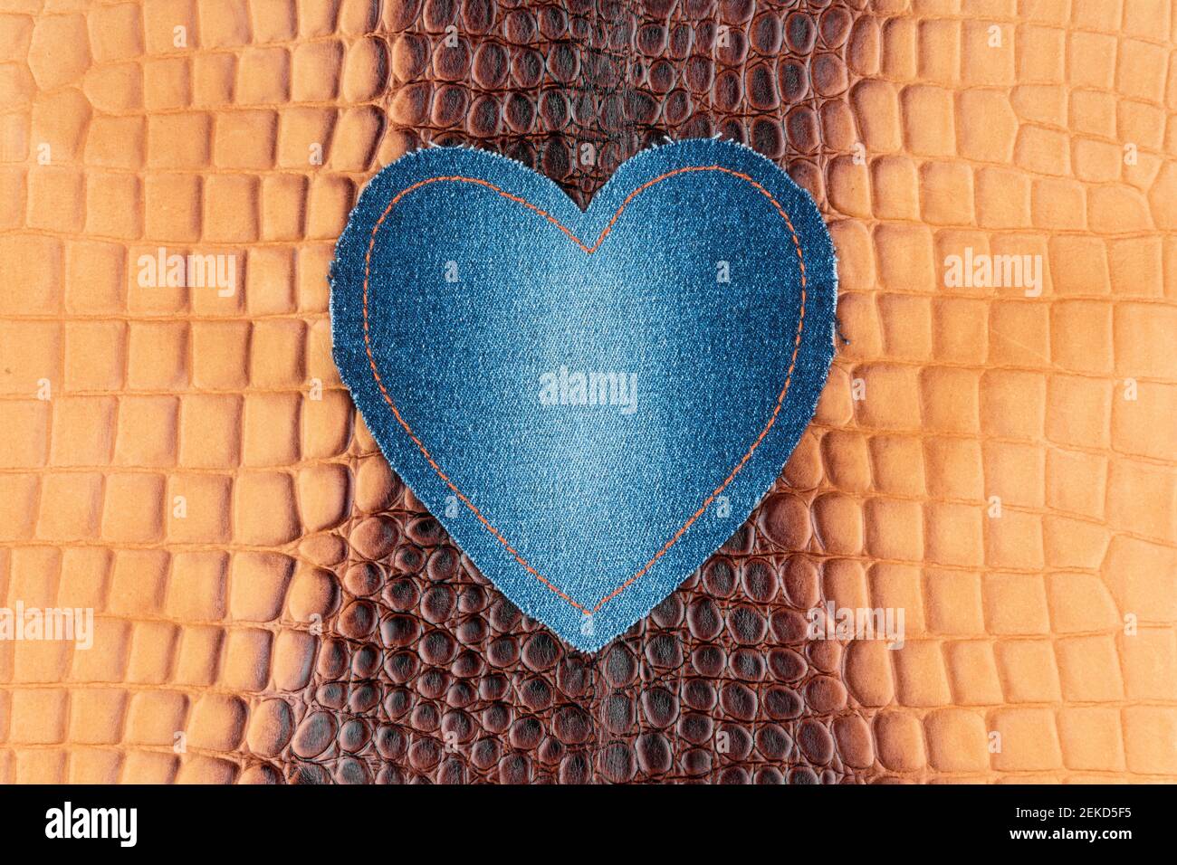 Il cuore in denim blu si trova sulla pelle di coccodrillo marrone. Vista dall'alto Foto Stock