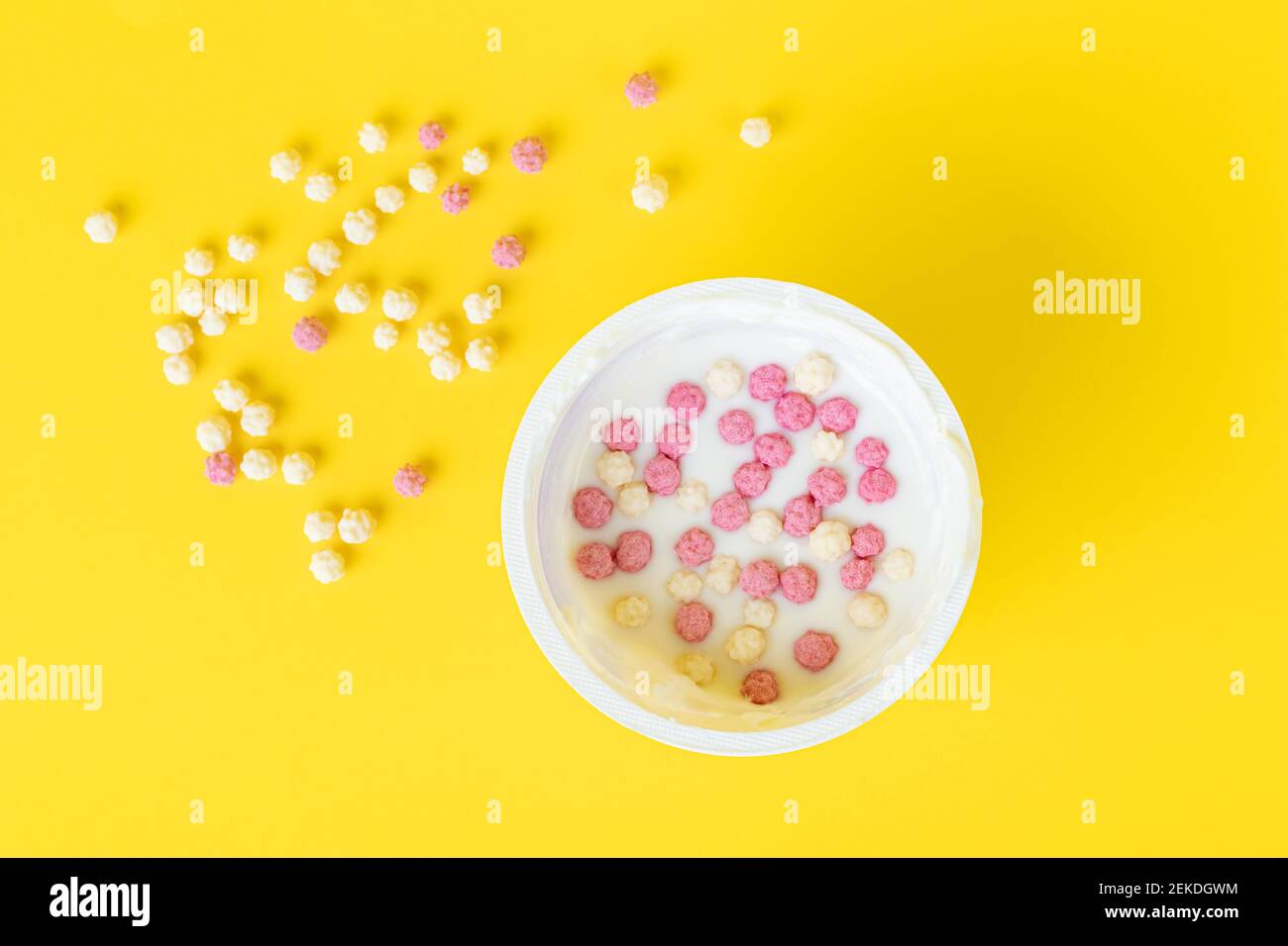 Yogurt in una tazza di plastica con fiocchi croccanti, cereali. Vista dall'alto. Sfondo giallo. Mattina, concetto di colazione Foto Stock