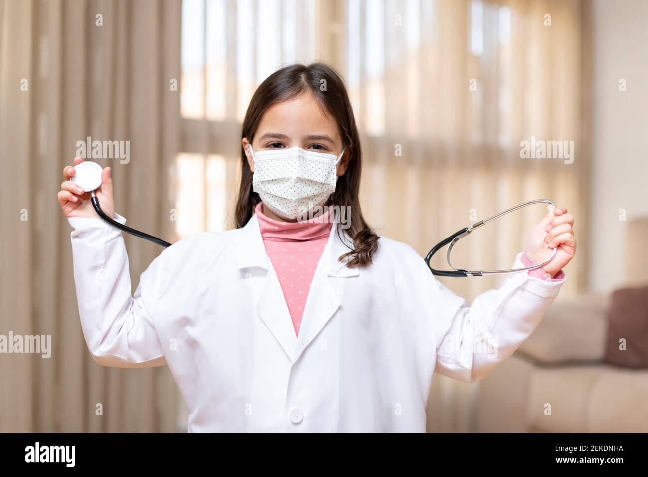 Ritratto di bambino che finge di essere un medico che gioca con uno stetoscopio. Indossa una maschera medica. Spazio per il testo. Foto Stock