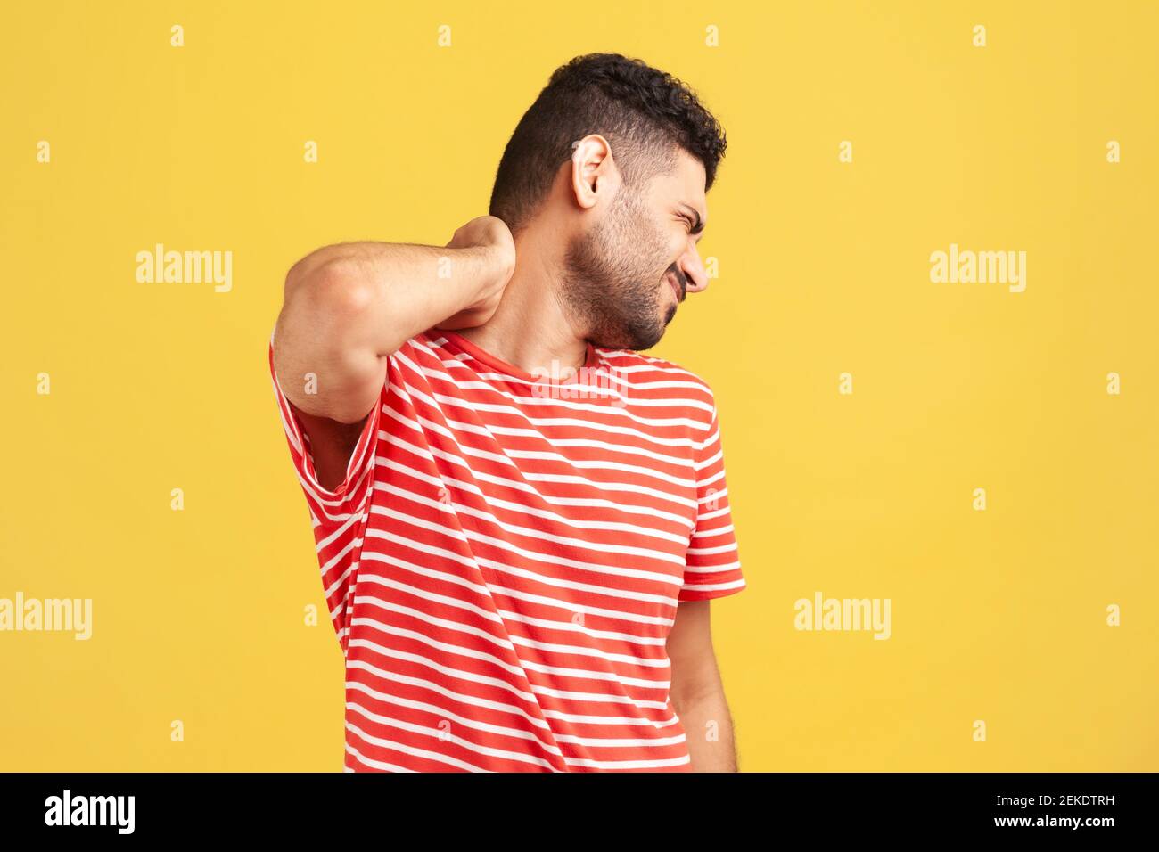Uomo ansioso sopportato in t-shirt a righe che tocca il collo, sensazione di dolore acuto che si muove e gira la testa, problemi alla spina dorsale, osteocondrosi. IO Foto Stock