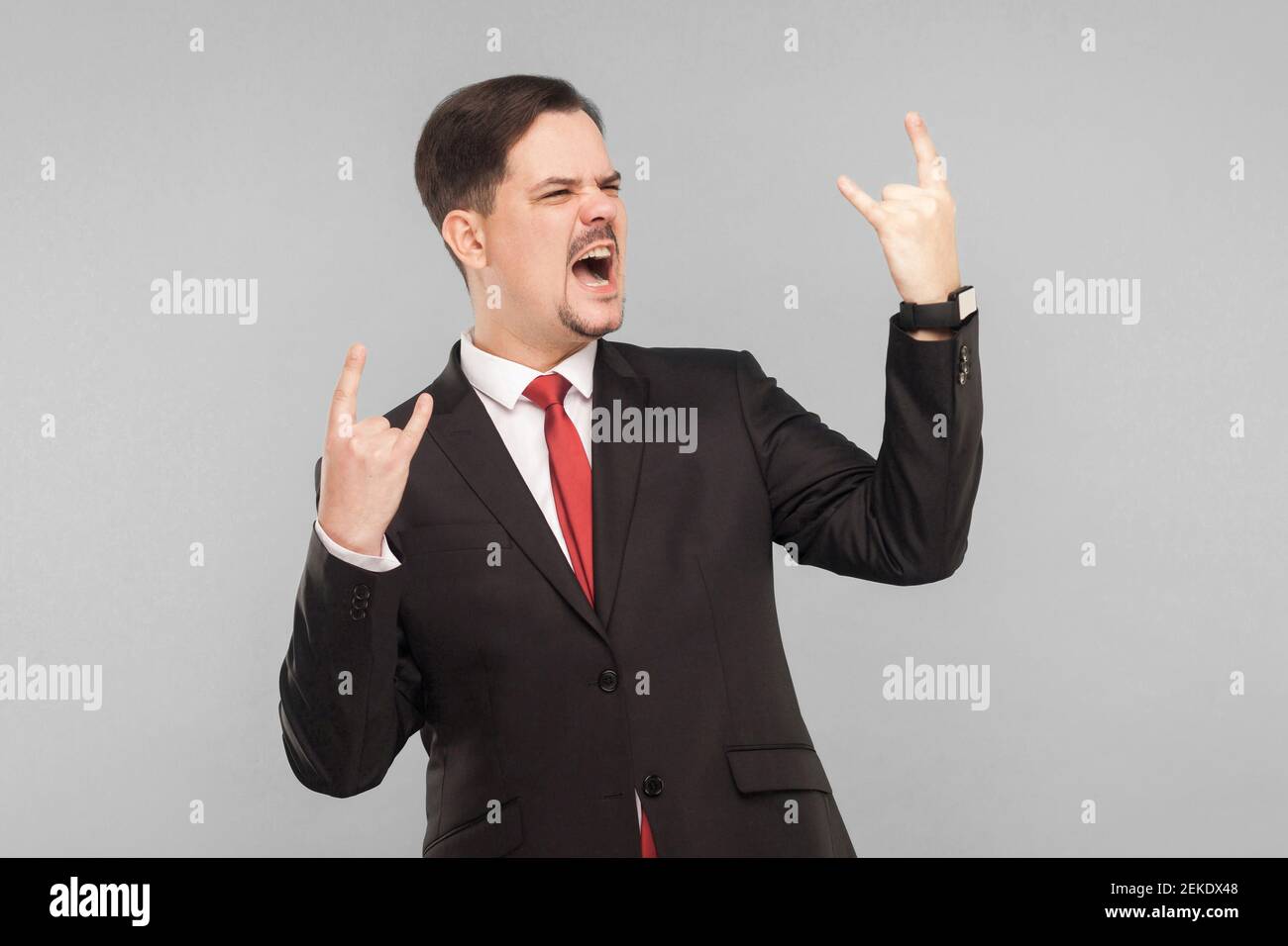 Felicità uomo attraente in stile classico ascolta la rock band preferita e canta con il film Indoor . interno studio girato. Isolato su sfondo grigio. Mani Foto Stock