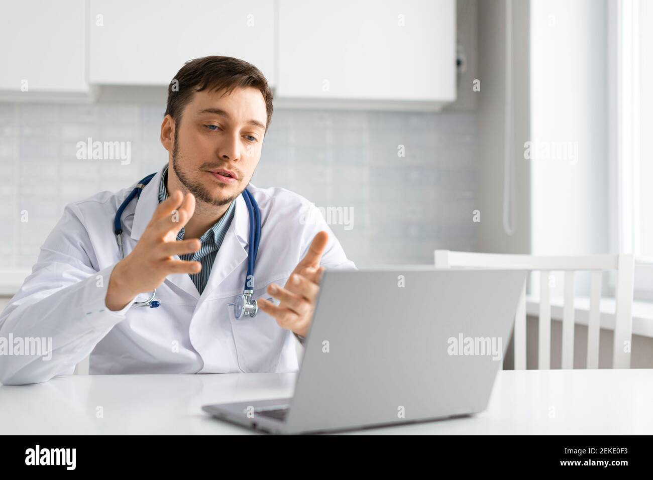 Medico durante una videochiamata online. Si siede al tavolo e parla con il paziente tramite collegamento video davanti a un monitor portatile. Concetto di tecnologia moderna Foto Stock
