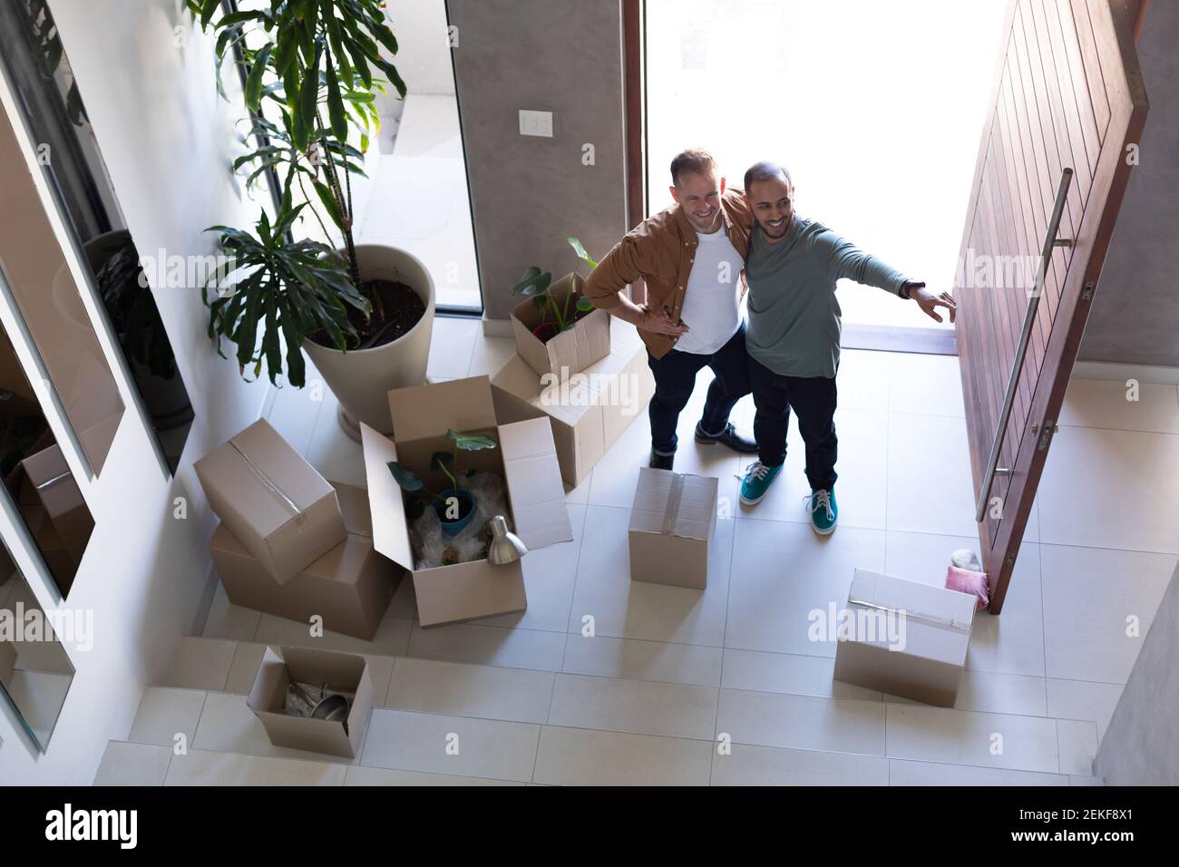 Multi etnico gay maschio coppia aprire porte anteriori e sorridente a casa Foto Stock