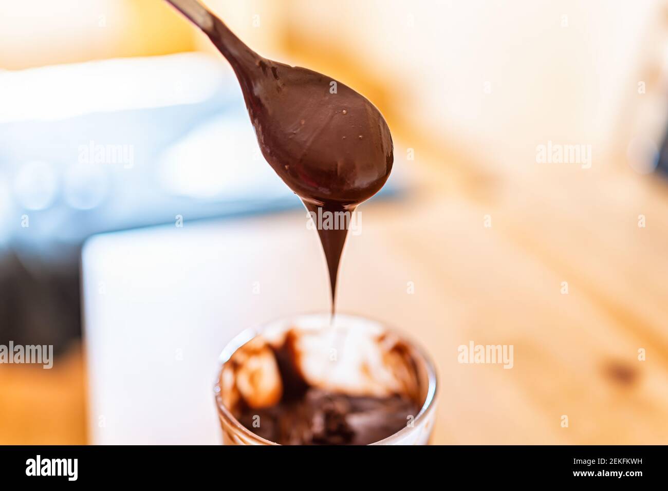Preparazione di un cucchiaio di salsa cremosa di nocciole di cioccolato liquido gocciolante mousse crema glassa con bokeh sfondo sfocato Foto Stock