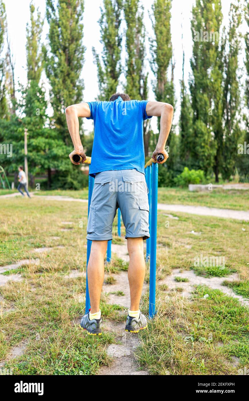 Fit giovane uomo che fa allenamento calistenico bilanciamento su barre orizzontali parallele esercizio in parco all'aperto a Rivne, Ucraina parco giochi vista verticale Foto Stock