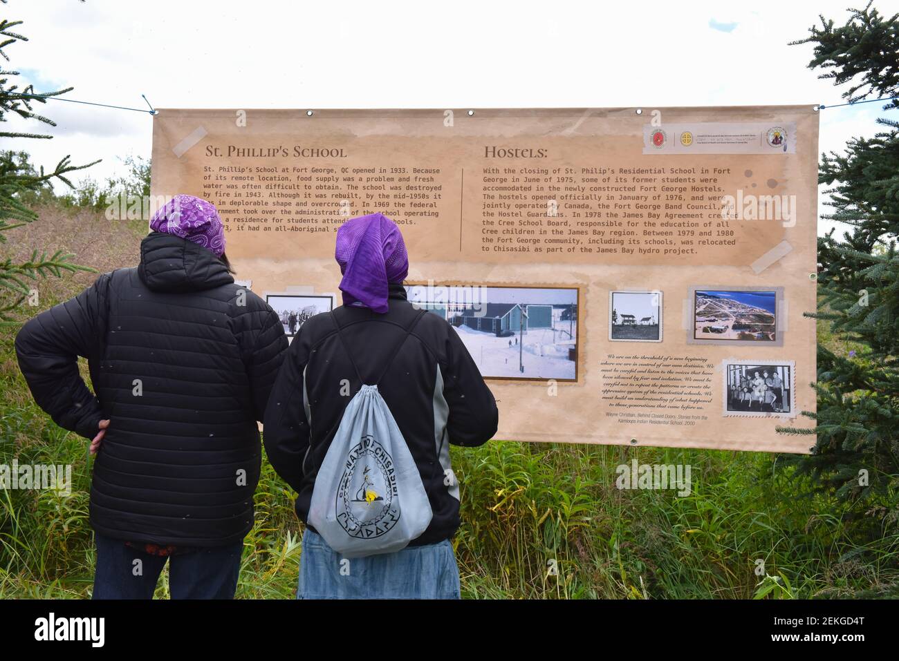 I sopravvissuti delle scuole residenziali indigene guardano i cartelloni esposti sul luogo in cui la scuola residenziale sull'isola di Fort George, James Bay, Quebec del Nord Canada Foto Stock