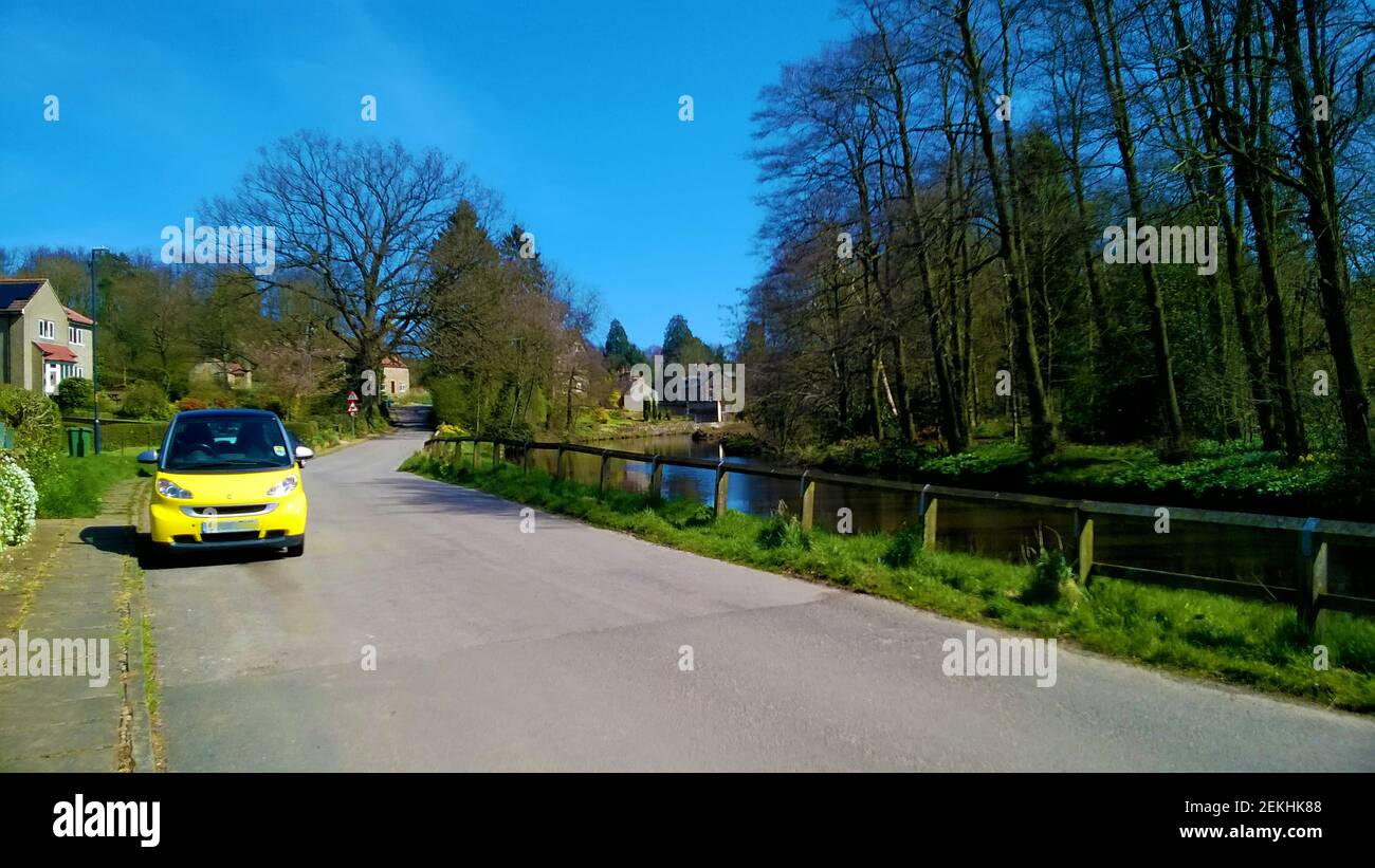 Un'auto gialla vicino a un ruscello di villaggio (thornton beck) a Thornton le Dale (aka Thornton Dale), vicino Pickering, Nord, Yorkshire. Thornton-le-Dale (un tempo noto come Torentune) è spesso considerato uno dei più belli dello Yorkshire. Era un tempo un telaio a mano tessitura cittadina ed è vicino alla foresta di Dalby. E l'antica chiesa sassone / normanna di St Hilda Ellerburn. Foto Stock