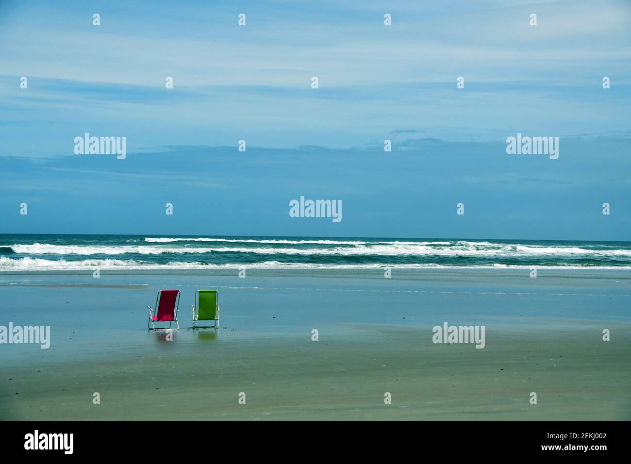 Una sedia da spiaggia verde e rossa di fronte all'oceano sulla spiaggia Foto Stock