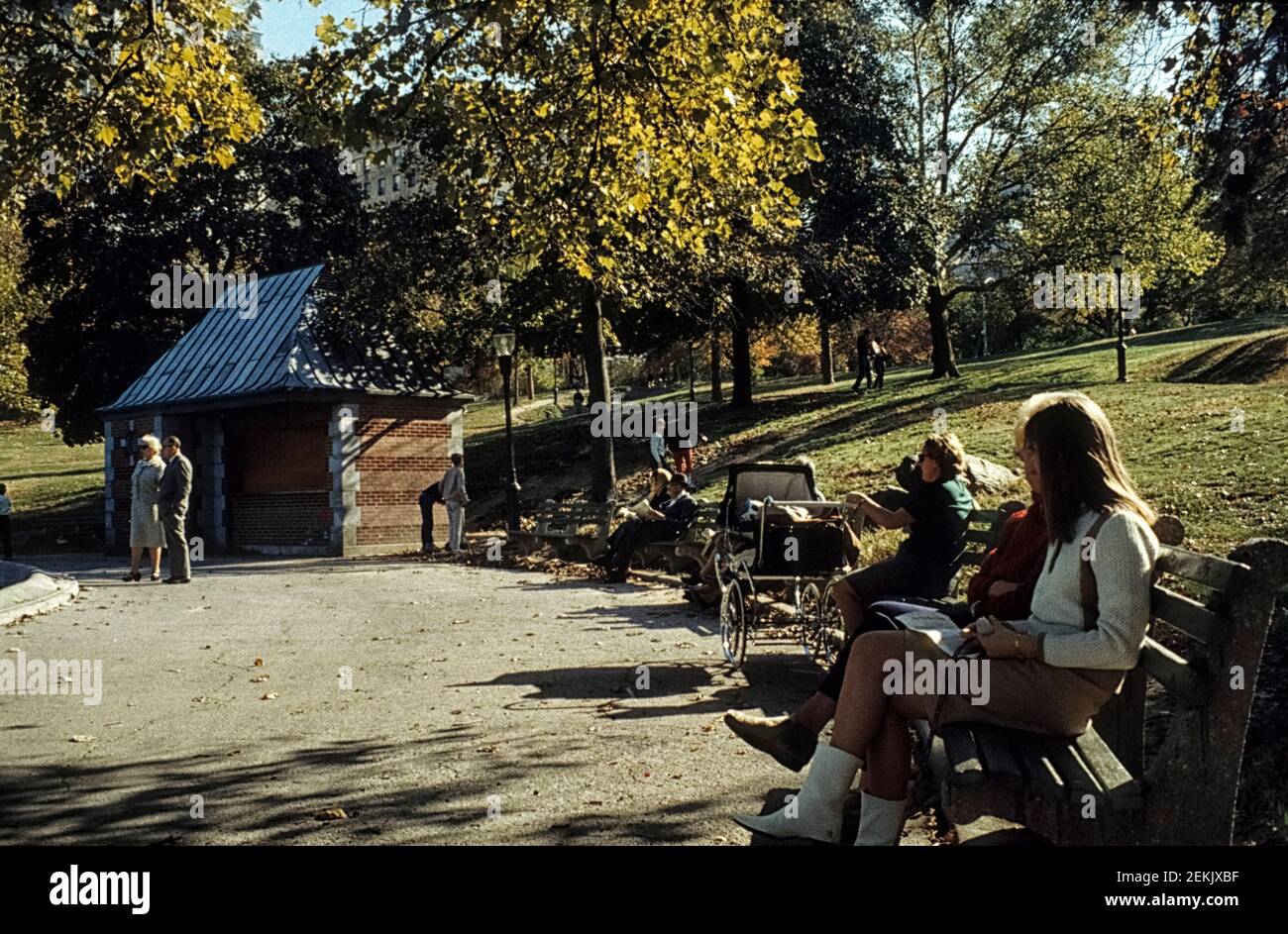 Persone sedute su panchine in legno e cemento di New York che godono del sole d'autunno. Central Park, Manhattan, New York City, Stati Uniti, 1965 Foto Stock