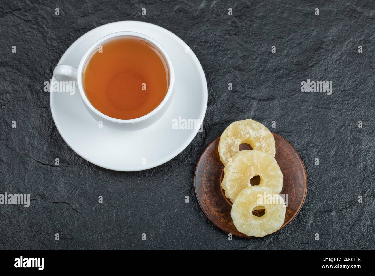 Una tazza di tè aromatico con ananas secco su sfondo scuro. Foto di alta qualità Foto Stock
