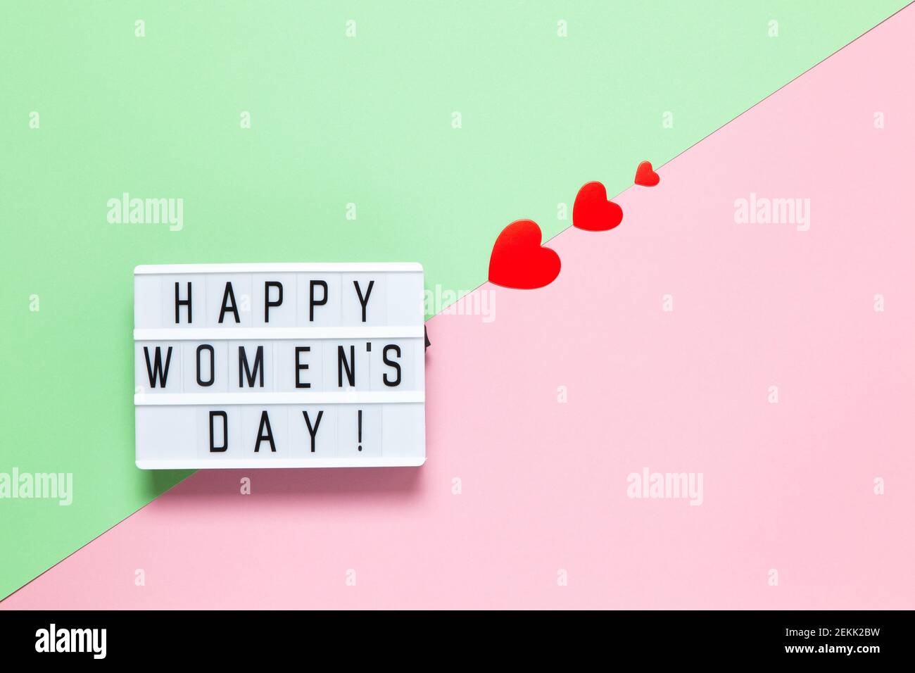 Lavagna luminosa con iscrizione Happy Women's Day, tre cuori rossi di diverse dimensioni su sfondo pastello rosa e verde, spazio copia. Orizzontale. Aeroporto internazionale Foto Stock