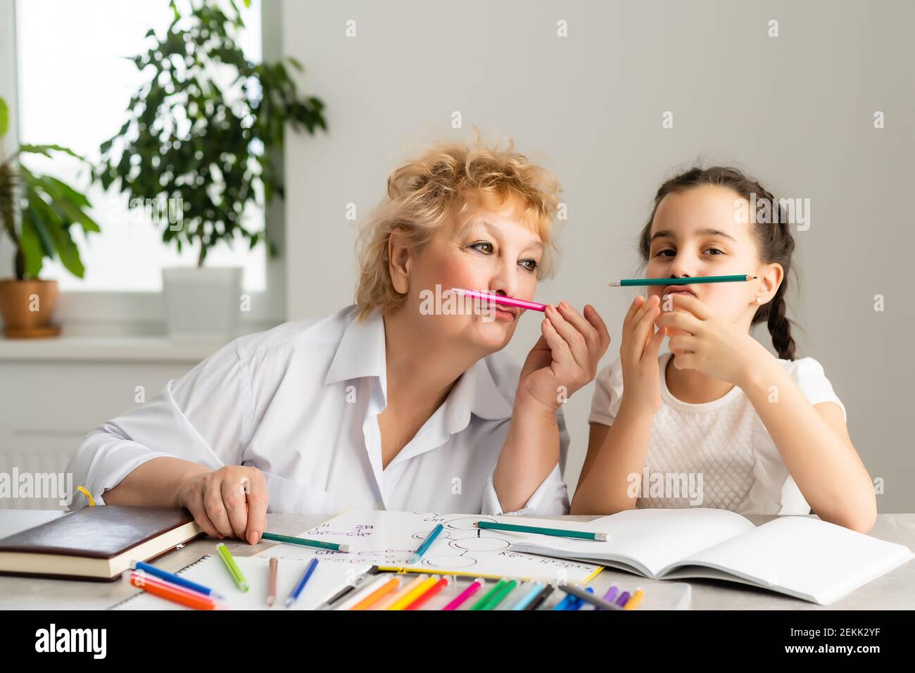 Felice nipote con nonna che si diverte, disegnando matite colorate, sedendosi insieme a casa, ridendo ragazza prescolare con sorridente pittura nonna Foto Stock