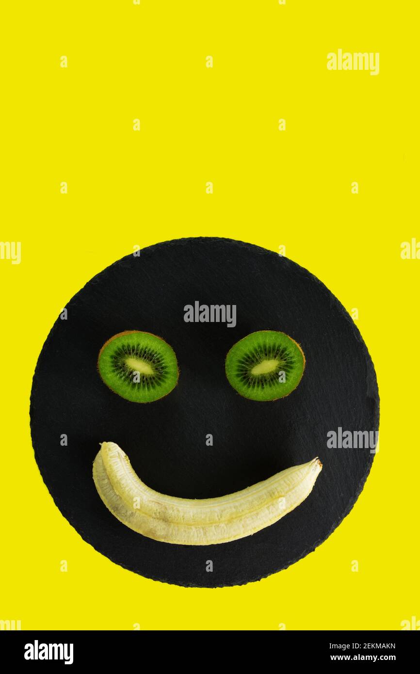 Metà Kiwi e una banana sbucciata su vassoio nero e. sfondo giallo Foto Stock