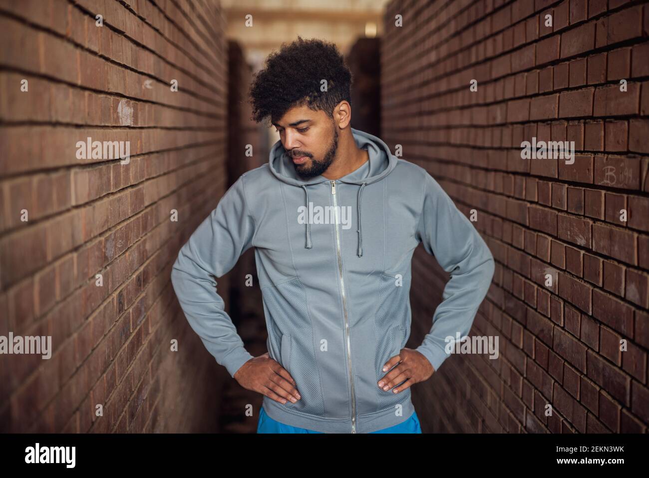 Ritratto di un giovane afro-americano molto animato in piedi all'interno del luogo abbandonato nel mezzo di due muri e pensare Foto Stock