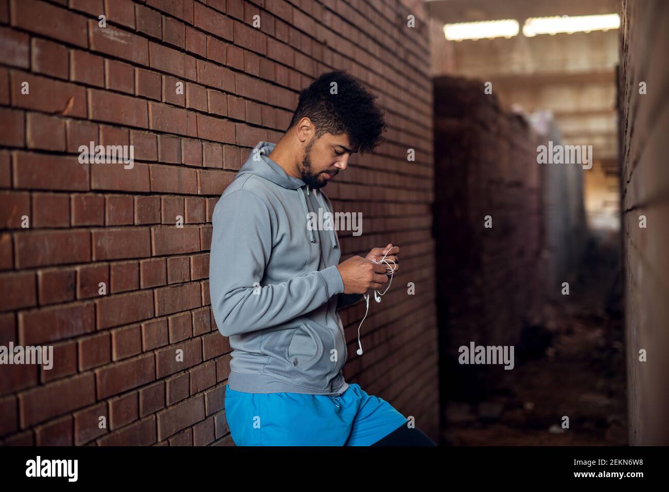 Ritratto di un giovane afro-americano molto animato in piedi all'interno del luogo abbandonato nel mezzo di due pareti preparazione ea Foto Stock