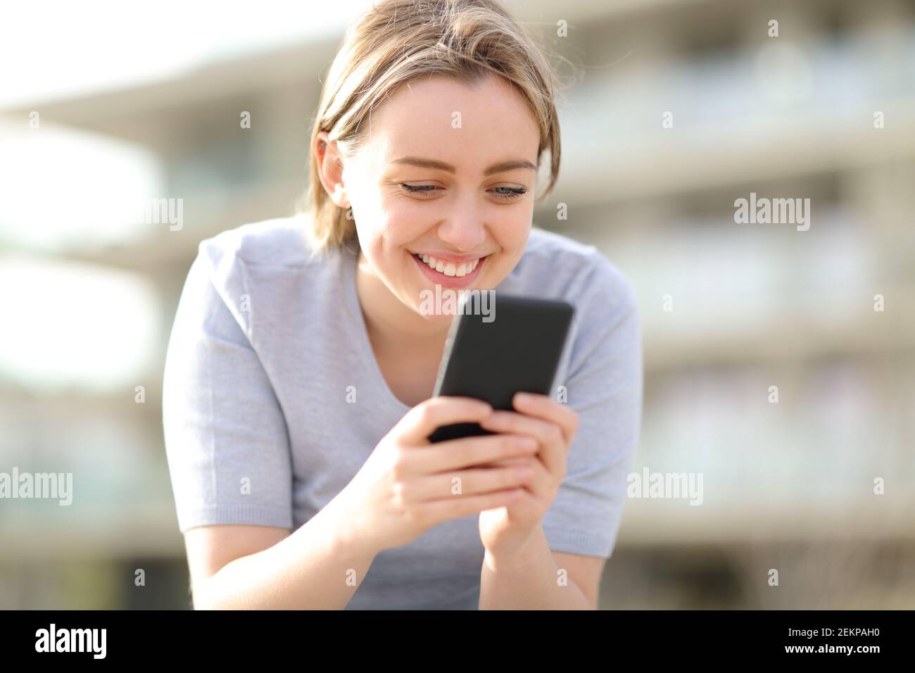 Felice singolo teen utilizzando smart phone sititng in strada una giornata di sole Foto Stock