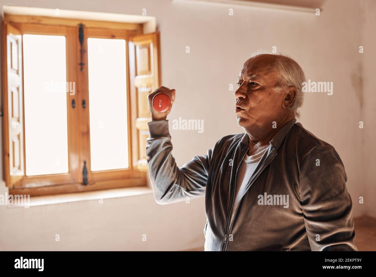 Un uomo anziano sta facendo gli esercizi di stretching e di peso a casa sua Foto Stock