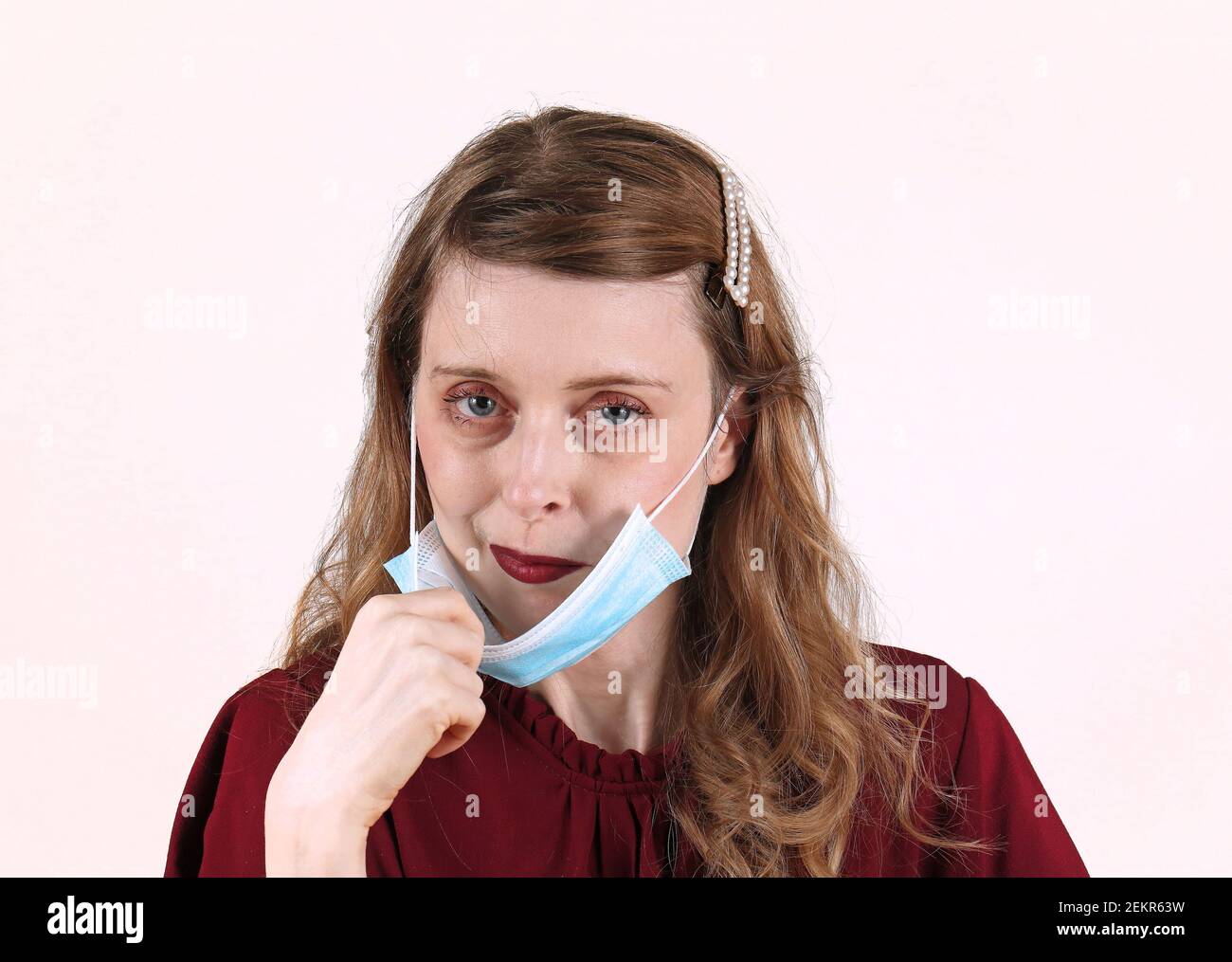 Giovane bella donna con rossetto rosso scuro che tette via medico maschera protettiva Foto Stock