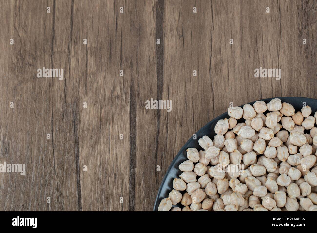 Una piastra scura piena di piselli bianchi secchi un tavolo di legno Foto Stock