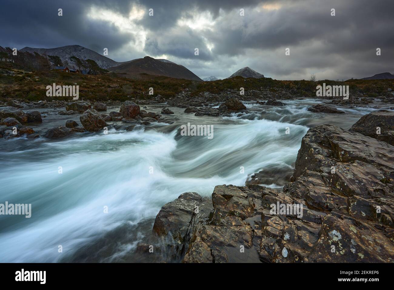 Lunga esposizione di acqua con rocce in primo piano, vegetazione invernale sul fiume Sligachan sull'isola di Skye Scozia con la montagna Cuillin r Foto Stock