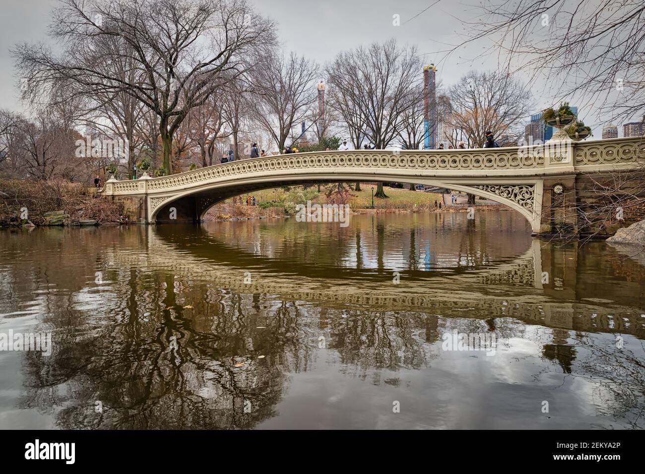 Il ponte di prua nel parco centrale, vista della luce naturale di New York in inverno con riflessi in acqua, nuvole, alberi e skyline di Manhattan sullo sfondo Foto Stock
