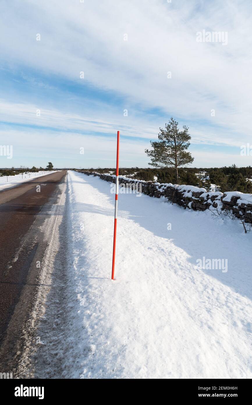 Strada di campagna diritta con un palanchetto di neve rosso a lato della strada Foto Stock