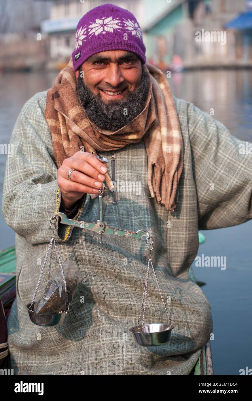 Srinagar, Jammu e Kashmir, India - 1 gennaio 2015: Il venditore di tè che indossa il ferano sul lago di dal pesa un sacchetto di tè mentre nella sua barca Foto Stock