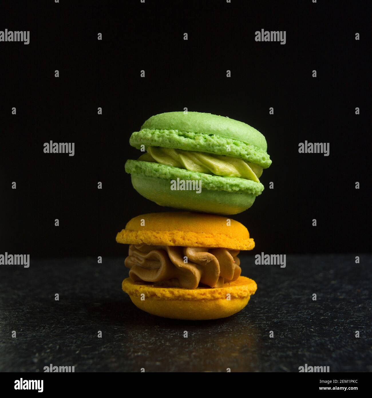 Macaron colorati impilati su una superficie scura, che evidenziano vivaci sapori verdi e gialli in una disposizione semplice Foto Stock