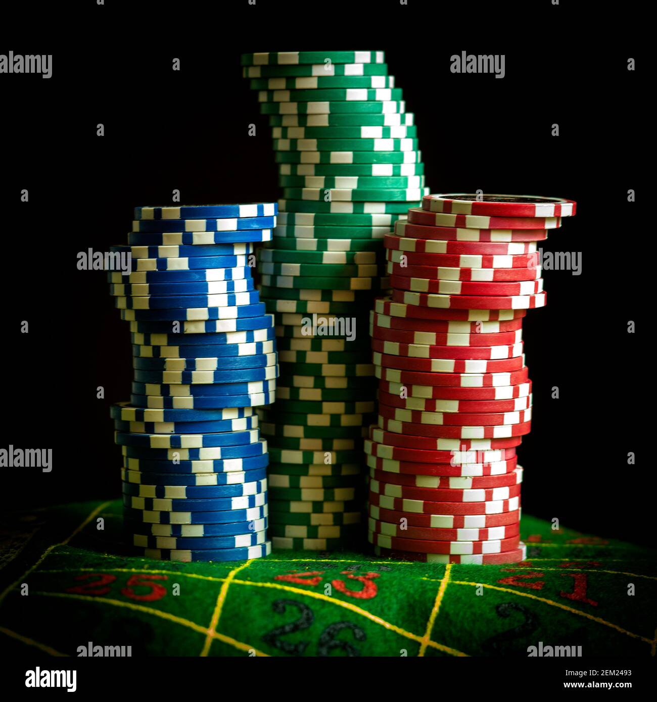 Gettoni da poker impilati in blu, verde e rosso su un tavolo del casinò pronti per una partita di notte Foto Stock
